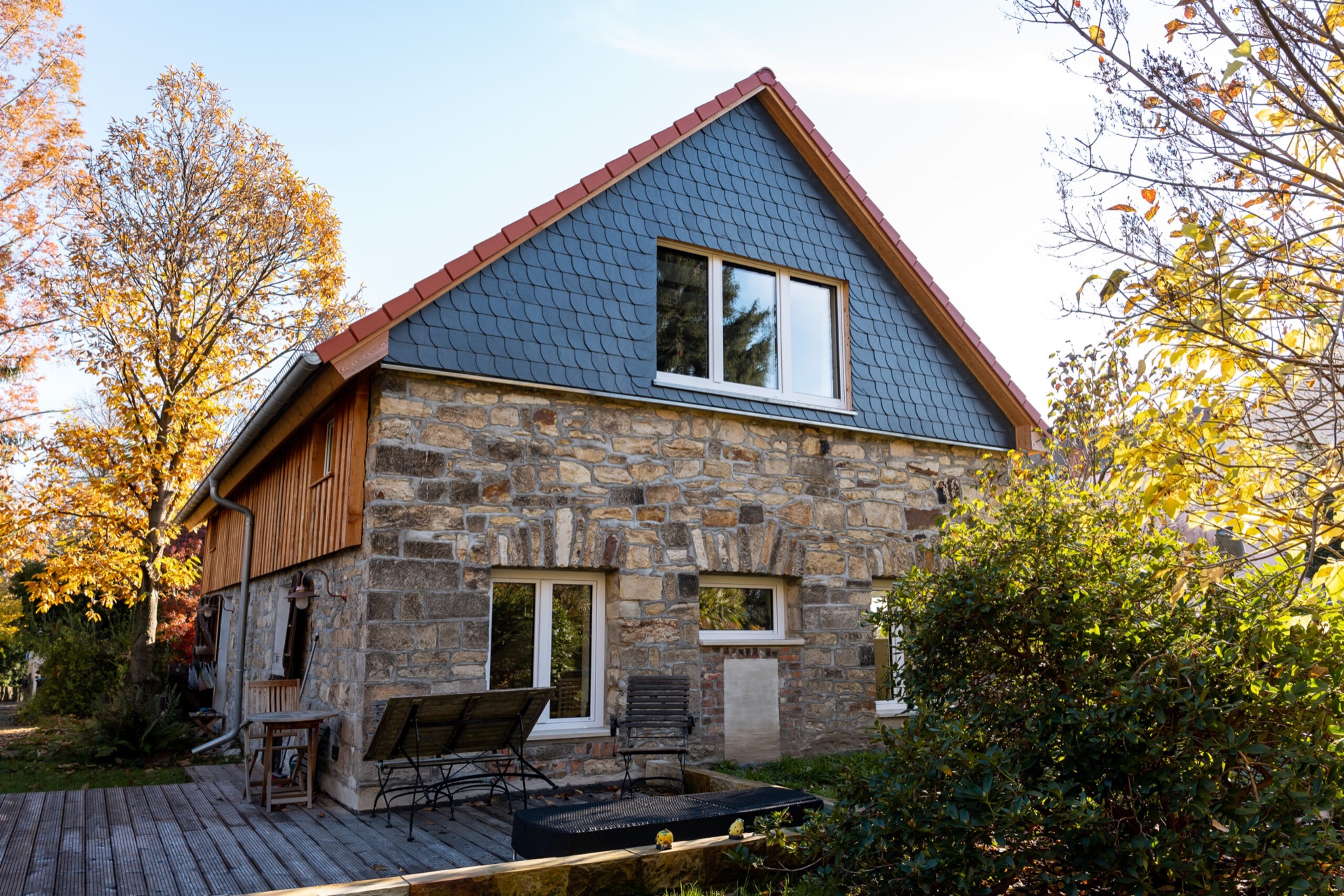 Zum Wohnhaus umgebaute Scheune mit Bruchsteinmauern, Schiefergiebel und Holzterrasse