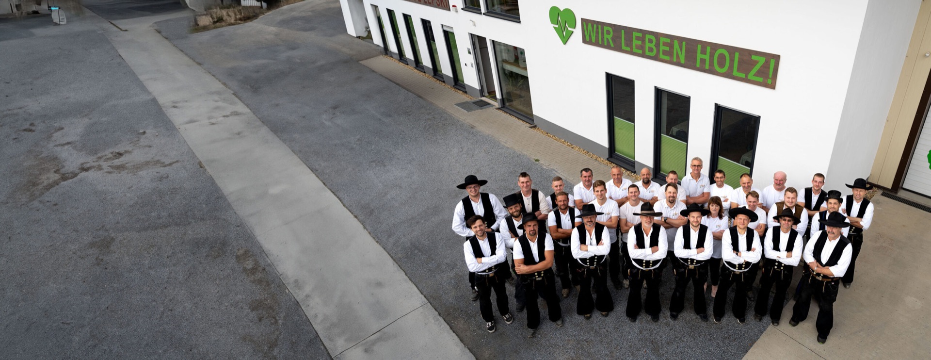 Das Team der Holzbau Lepski GmbH vor dem Firmengebäude in Dresden-Reick, vorn in Zimmermannskluft, an der Wand der Schriftzug „Wir leben Holz!“